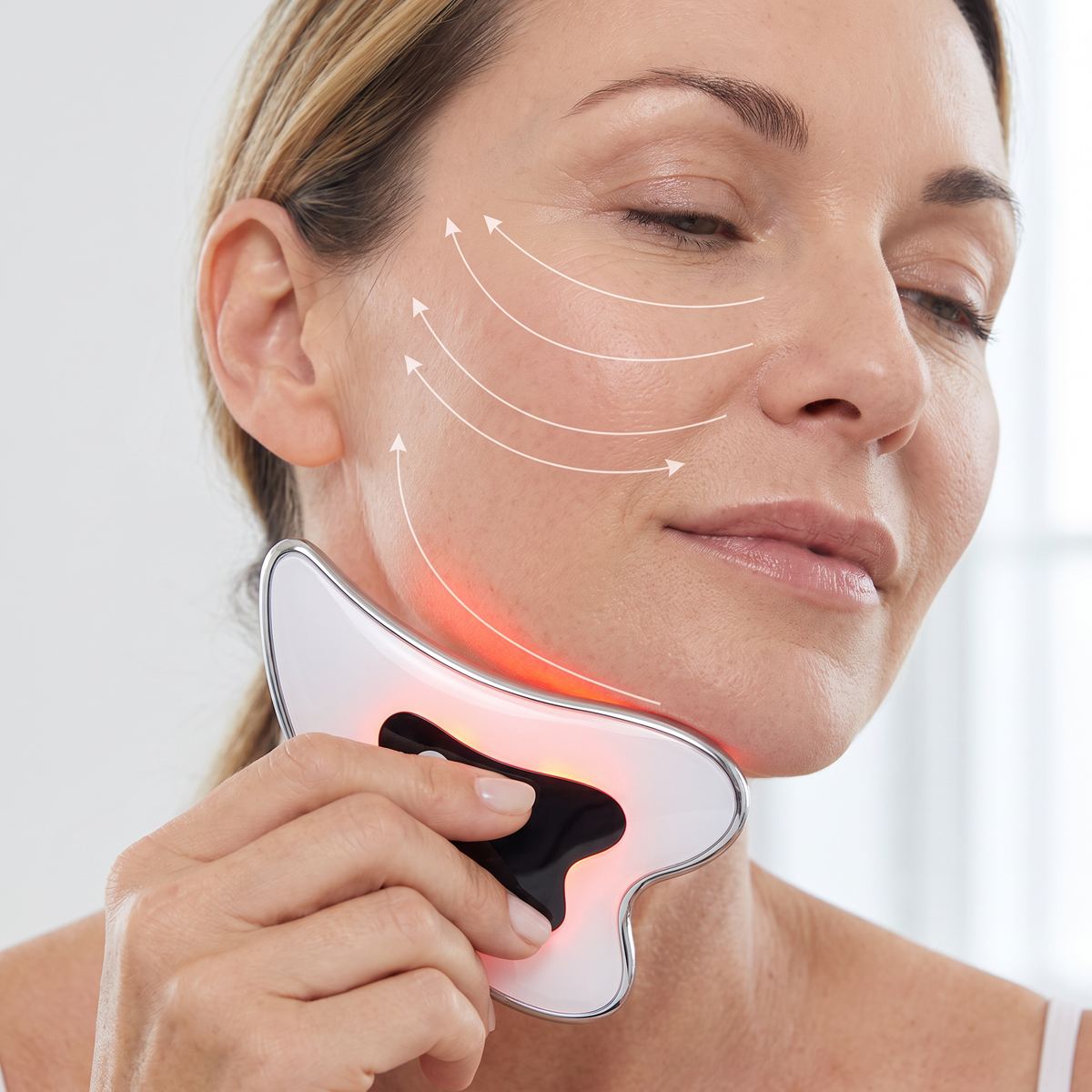 A woman gliding the device along her jaw with the red light on, arrows showing the upward strokes